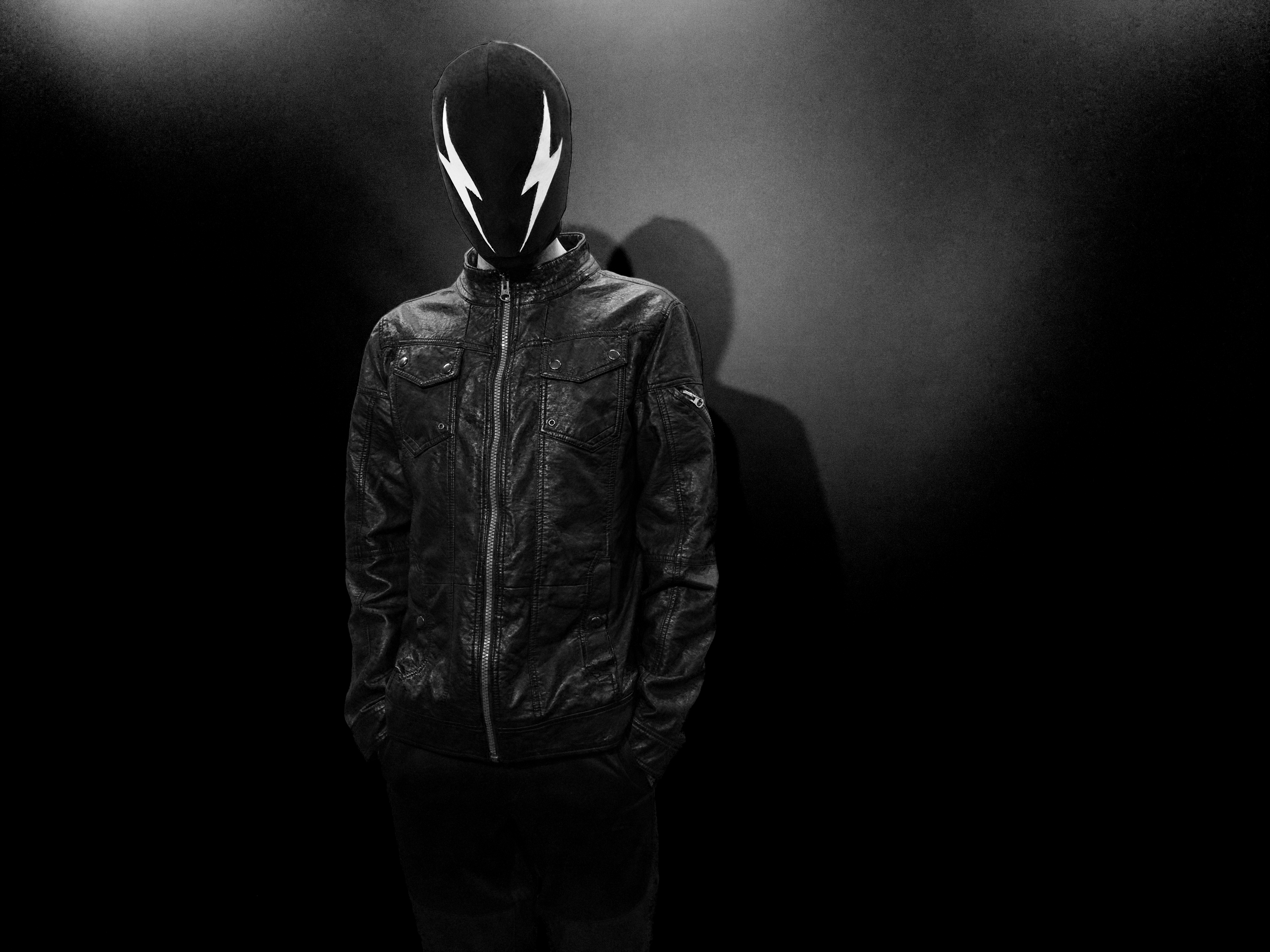ECTRIK — a masked figure in a black leather jacket with a white lightning-bolt motif across the face, lit by a dramatic spotlight against a dark background.
